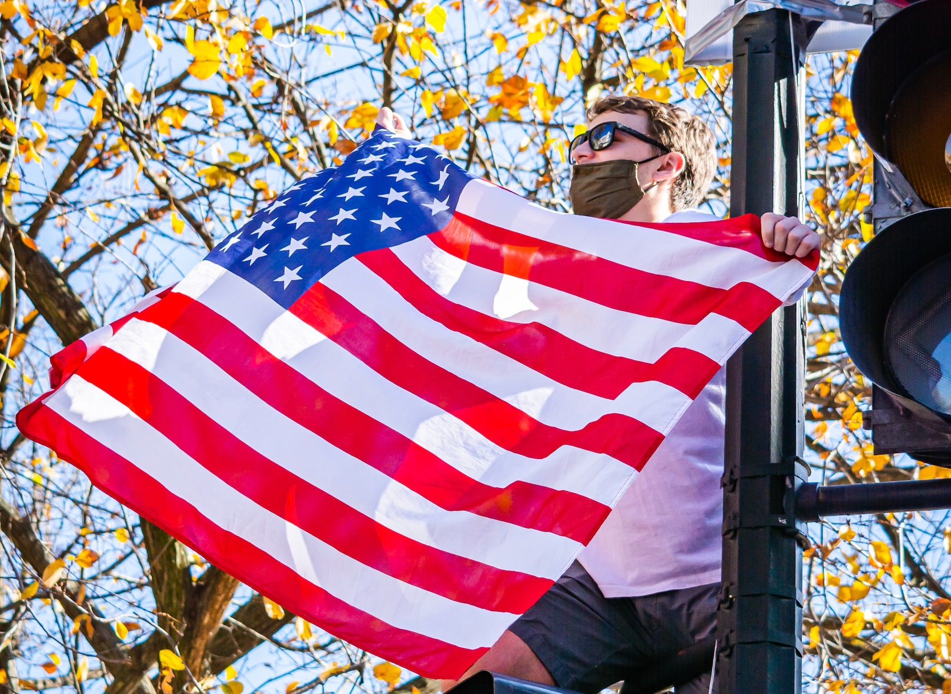 Man Holding US flag on a traffic light | Veteran Car Donations