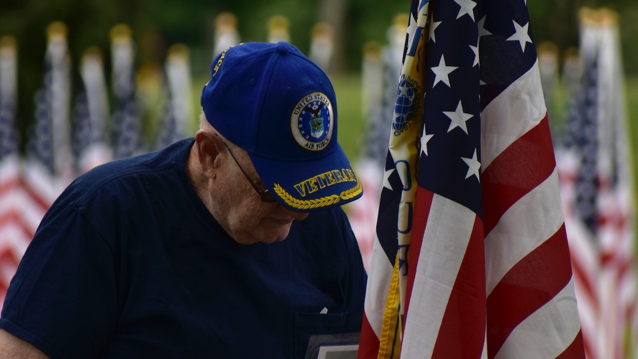 An Elderly Man Standing Beside an American Flag | Veteran Car Donations
